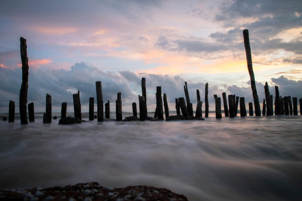 Breathtaking sunset over the ocean with weathered posts emerging from the waves at Tajpur Beach, India.